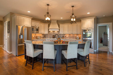Example of a mid-sized transitional l-shaped medium tone wood floor eat-in kitchen design in Cincinnati with a drop-in sink, raised-panel cabinets, beige cabinets, granite countertops, beige backsplash, ceramic backsplash, stainless steel appliances and an island