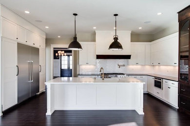This is an example of a mid-sized transitional u-shaped separate kitchen in Louisville with a farmhouse sink, shaker cabinets, white cabinets, white splashback, subway tile splashback, stainless steel appliances, dark hardwood floors, with island, brown floor and black benchtop.