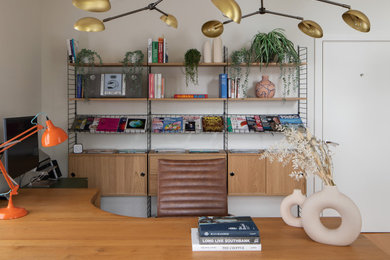 Large midcentury study in Kent with white walls, light hardwood flooring, a built-in desk and feature lighting.