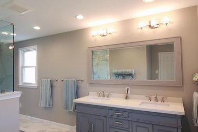 Example of a large beach style master white tile and porcelain tile porcelain tile and white floor double shower design in Philadelphia with furniture-like cabinets, gray cabinets, a two-piece toilet, beige walls, an undermount sink, marble countertops, a hinged shower door and white countertops