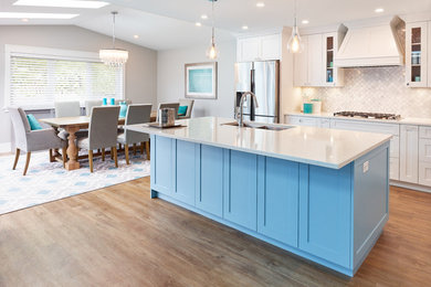 Photo of a beach style open plan kitchen in Vancouver with a drop-in sink, shaker cabinets, black cabinets, quartz benchtops, grey splashback, mosaic tile splashback, stainless steel appliances, vinyl floors, with island and white benchtop.