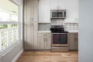 Example of a mid-sized transitional l-shaped light wood floor open concept kitchen design in Miami with a double-bowl sink, shaker cabinets, white cabinets, quartz countertops, gray backsplash, ceramic backsplash, stainless steel appliances and a peninsula
