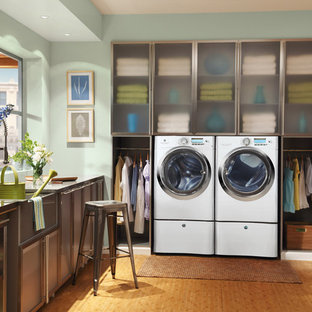 Modelo de lavadero multiusos y en L, clásico renovado, de tamaño medio, con fregadero sobremueble, armarios tipo vitrina, puertas de armario en acero inoxidable, encimera de acero inoxidable, paredes verdes, suelo de madera en tonos medios y lavadora y secadora juntas