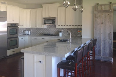 Mid-sized transitional l-shaped eat-in kitchen in Phoenix with grey splashback, a double-bowl sink, shaker cabinets, white cabinets, ceramic splashback, stainless steel appliances, dark hardwood floors and a peninsula.