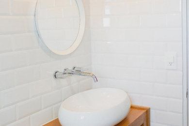 Minimalist white tile and subway tile ceramic tile and brown floor bathroom photo with brown cabinets, white walls, a wall-mount sink, wood countertops and brown countertops