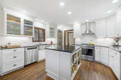 Eat-in kitchen - mid-sized transitional u-shaped vinyl floor and brown floor eat-in kitchen idea in Cleveland with a farmhouse sink, shaker cabinets, white cabinets, quartz countertops, white backsplash, subway tile backsplash, stainless steel appliances, an island and black countertops