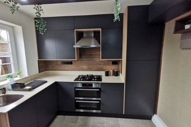 Photo of a small modern cream and black u-shaped kitchen/diner in London with an integrated sink, black cabinets, composite countertops, multi-coloured splashback, ceramic splashback, black appliances, vinyl flooring, no island, grey floors, beige worktops, a drop ceiling and a feature wall.
