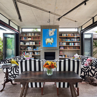 Bild på ett funkis vardagsrum, med tegelgolv, ett bibliotek, en standard öppen spis och en spiselkrans i tegelsten