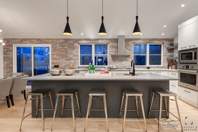 Inspiration for a contemporary l-shaped light wood floor eat-in kitchen remodel in Calgary with a drop-in sink, flat-panel cabinets, white cabinets, brick backsplash, stainless steel appliances, an island and gray countertops