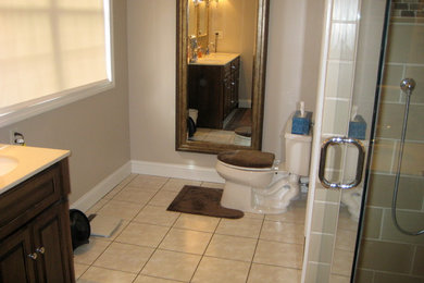 Mid-sized master beige tile and ceramic tile ceramic tile alcove shower photo in New York with an integrated sink, raised-panel cabinets, dark wood cabinets, solid surface countertops, a one-piece toilet and beige walls