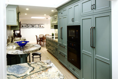 Example of a mid-sized classic galley light wood floor kitchen pantry design in San Francisco with a double-bowl sink, flat-panel cabinets, green cabinets, granite countertops, brown backsplash, glass tile backsplash, paneled appliances and a peninsula