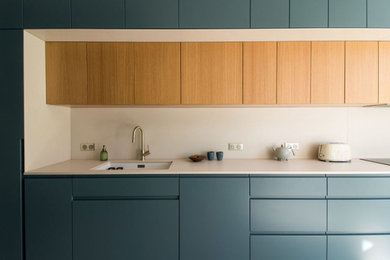 Photo of a large contemporary enclosed kitchen in Paris with a submerged sink, beaded cabinets, blue cabinets, composite countertops, white splashback, ceramic splashback, ceramic flooring, beige floors and white worktops.
