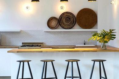 Open concept kitchen - large contemporary u-shaped light wood floor and beige floor open concept kitchen idea in New York with wood countertops, flat-panel cabinets, white backsplash, subway tile backsplash, paneled appliances, a peninsula, a drop-in sink, white cabinets and brown countertops