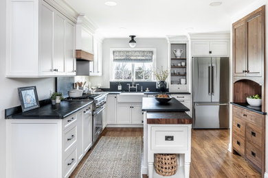 Mid-sized transitional l-shaped medium tone wood floor and brown floor eat-in kitchen photo in Philadelphia with a farmhouse sink, shaker cabinets, gray cabinets, soapstone countertops, black backsplash, stone slab backsplash, stainless steel appliances, an island and black countertops