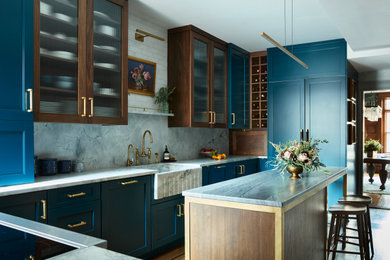 Example of a mid-sized transitional u-shaped dark wood floor and brown floor kitchen design in Boston with a farmhouse sink, recessed-panel cabinets, blue cabinets, quartzite countertops, gray backsplash, stone slab backsplash, paneled appliances, an island and gray countertops