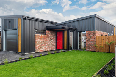 Photo of a small modern one-storey black house exterior in Christchurch with metal siding, a butterfly roof, a metal roof and a black roof.