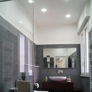 Photo of a mid-sized modern 3/4 bathroom in Other with flat-panel cabinets, red cabinets, a corner shower, a wall-mount toilet, gray tile, porcelain tile, grey walls, laminate floors, a vessel sink, grey floor, an open shower, red benchtops, a single vanity and a floating vanity.