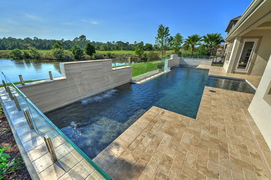 This is an example of a mid-sized modern backyard rectangular pool in Orlando with a water feature and natural stone pavers.
