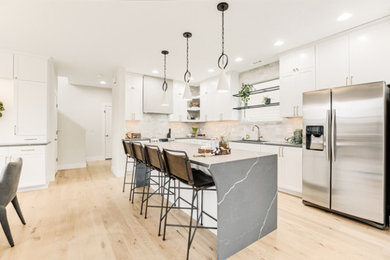 Example of a mid-sized minimalist light wood floor and beige floor open concept kitchen design in Portland with an undermount sink, shaker cabinets, white cabinets, quartz countertops, gray backsplash, limestone backsplash, stainless steel appliances, an island and gray countertops