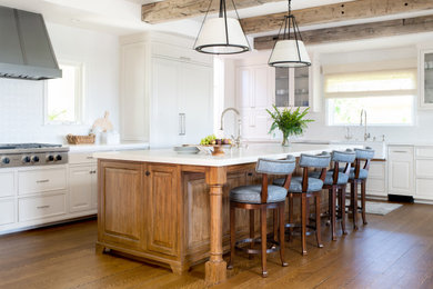 Design ideas for a large country u-shaped eat-in kitchen in Los Angeles with a farmhouse sink, raised-panel cabinets, white cabinets, quartzite benchtops, white splashback, mosaic tile splashback, panelled appliances, dark hardwood floors, with island, brown floor, white benchtop and exposed beam.