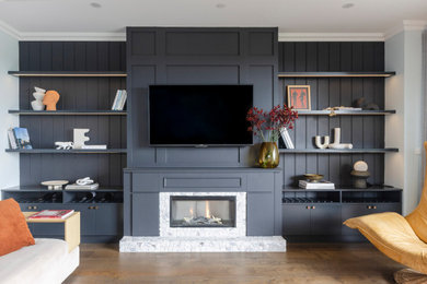 Design ideas for a mid-sized traditional open concept living room with a library, black walls, dark hardwood floors, a standard fireplace, a stone fireplace surround, a built-in media wall, brown floor and decorative wall panelling.