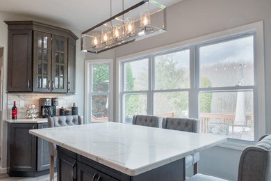 Mid-sized vinyl floor and beige floor eat-in kitchen photo in New York with recessed-panel cabinets, gray cabinets, quartz countertops, white backsplash, ceramic backsplash, stainless steel appliances, an island, white countertops and an undermount sink