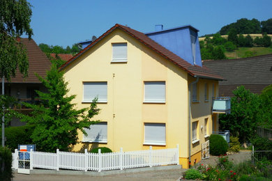 This is an example of a mid-sized contemporary three-storey stucco yellow house exterior in Frankfurt with a gable roof and a tile roof.