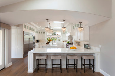 Huge transitional u-shaped medium tone wood floor, brown floor and coffered ceiling eat-in kitchen photo in Santa Barbara with an undermount sink, raised-panel cabinets, white cabinets, marble countertops, white backsplash, marble backsplash, stainless steel appliances, an island and white countertops