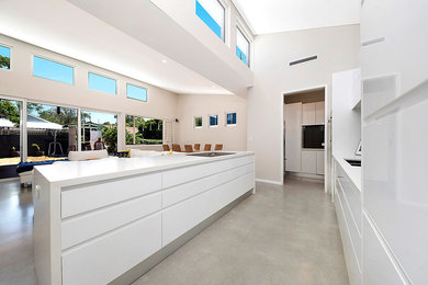 Inspiration for a mid-sized contemporary galley open plan kitchen in Perth with an undermount sink, flat-panel cabinets, white cabinets, quartz benchtops, grey splashback, glass sheet splashback, stainless steel appliances, concrete floors, with island, grey floor and white benchtop.