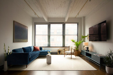 Modelo de salón tipo loft urbano de tamaño medio con paredes grises, suelo de madera en tonos medios, televisor colgado en la pared, suelo marrón y vigas vistas