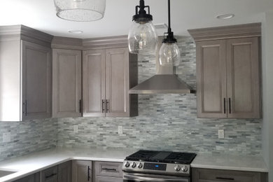 Mid-sized beach style l-shaped medium tone wood floor and brown floor eat-in kitchen photo in New York with an undermount sink, shaker cabinets, gray cabinets, quartz countertops, multicolored backsplash, stone tile backsplash, stainless steel appliances, an island and white countertops