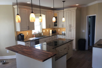 Example of a large transitional l-shaped porcelain tile and brown floor open concept kitchen design in Other with an undermount sink, raised-panel cabinets, distressed cabinets, marble countertops, beige backsplash, ceramic backsplash, stainless steel appliances, an island and brown countertops