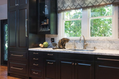 Inspiration for a mid-sized traditional galley separate kitchen in Sacramento with an undermount sink, black cabinets, marble benchtops, marble splashback, brown floor, raised-panel cabinets, multi-coloured splashback, panelled appliances, medium hardwood floors, with island and multi-coloured benchtop.