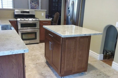 Eat-in kitchen - mid-sized modern u-shaped travertine floor and beige floor eat-in kitchen idea in San Diego with a farmhouse sink, shaker cabinets, brown cabinets, quartzite countertops, stainless steel appliances and a peninsula