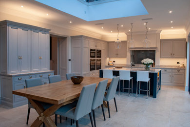 Large traditional open plan kitchen in Essex with a submerged sink, flat-panel cabinets, grey cabinets, marble worktops, mirror splashback, integrated appliances, travertine flooring, an island, beige floors, beige worktops, a vaulted ceiling and feature lighting.