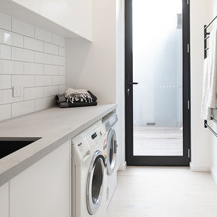 Medium sized contemporary single-wall separated utility room in Melbourne with a submerged sink, white cabinets, engineered stone countertops, white walls, light hardwood flooring, a side by side washer and dryer, grey worktops, flat-panel cabinets and beige floors.
