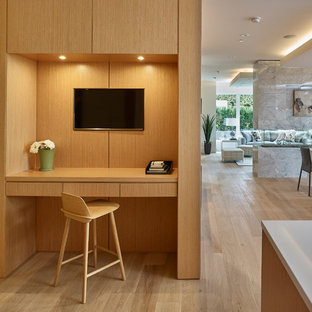 This is an example of a small modern home office and library in Vancouver with white walls, light hardwood flooring, a two-sided fireplace, a tiled fireplace surround, a built-in desk and beige floors.