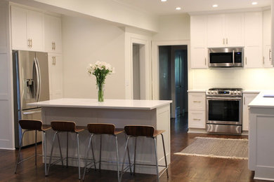 Inspiration for a mid-sized transitional u-shaped medium tone wood floor and brown floor open concept kitchen remodel in Kansas City with an undermount sink, shaker cabinets, white cabinets, solid surface countertops, white backsplash, glass tile backsplash, stainless steel appliances, an island and white countertops