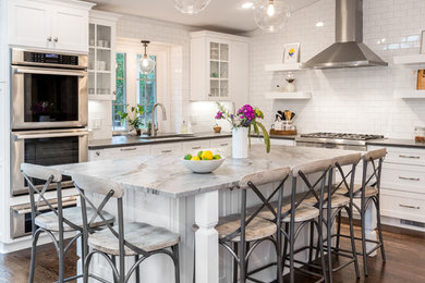 Inspiration for a transitional l-shaped dark wood floor and brown floor kitchen remodel in Detroit with an undermount sink, shaker cabinets, white cabinets, white backsplash, subway tile backsplash, stainless steel appliances, an island and black countertops