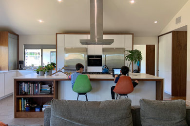 Mid-sized 1950s l-shaped porcelain tile, gray floor and vaulted ceiling open concept kitchen photo in San Diego with an undermount sink, flat-panel cabinets, white cabinets, quartz countertops, white backsplash, quartz backsplash, stainless steel appliances, an island and white countertops