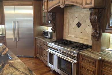 Inspiration for a mid-sized timeless l-shaped medium tone wood floor and brown floor kitchen remodel in Orange County with dark wood cabinets, beige backsplash, stone tile backsplash, stainless steel appliances, an island and recessed-panel cabinets