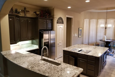 Inspiration for a mid-sized timeless l-shaped porcelain tile and gray floor open concept kitchen remodel in Dallas with an undermount sink, raised-panel cabinets, dark wood cabinets, granite countertops, gray backsplash, porcelain backsplash, stainless steel appliances, an island and gray countertops