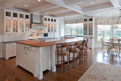 Large elegant medium tone wood floor and brown floor kitchen photo in New York with glass-front cabinets, white cabinets, gray backsplash, marble backsplash, stainless steel appliances and an island