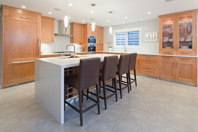 This is an example of a large contemporary l-shaped eat-in kitchen in Vancouver with a double-bowl sink, shaker cabinets, light wood cabinets, white splashback, panelled appliances, ceramic floors and with island.