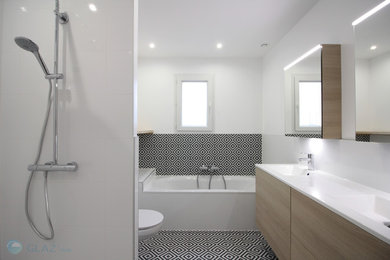 Mid-sized contemporary master bathroom in Other with beaded inset cabinets, light wood cabinets, a drop-in tub, an alcove shower, a wall-mount toilet, white tile, ceramic tile, white walls, cement tiles, a drop-in sink, solid surface benchtops, black floor, a hinged shower door and white benchtops.