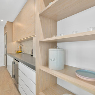 Zweizeilige, Große Moderne Küche mit Vorratsschrank, Einbauwaschbecken, profilierten Schrankfronten, hellen Holzschränken, Edelstahl-Arbeitsplatte, Küchenrückwand in Beige, Rückwand aus Keramikfliesen, Küchengeräten aus Edelstahl, hellem Holzboden, braunem Boden und grauer Arbeitsplatte in Auckland