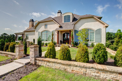 Example of a large transitional beige two-story brick house exterior design in Little Rock with a gambrel roof and a shingle roof