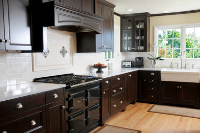 This is an example of a traditional l-shaped eat-in kitchen in Seattle with a farmhouse sink, glass-front cabinets, dark wood cabinets, marble benchtops, white splashback, subway tile splashback and black appliances.