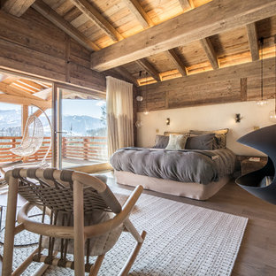 Cette photo montre une grande chambre parentale montagne avec un mur beige, un sol en bois brun, cheminée suspendue et un manteau de cheminée en métal.