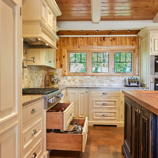 Photo of a large country u-shaped kitchen pantry in Other with a farmhouse sink, raised-panel cabinets, grey cabinets, wood benchtops, beige splashback, travertine splashback, panelled appliances, porcelain floors, with island and brown floor.